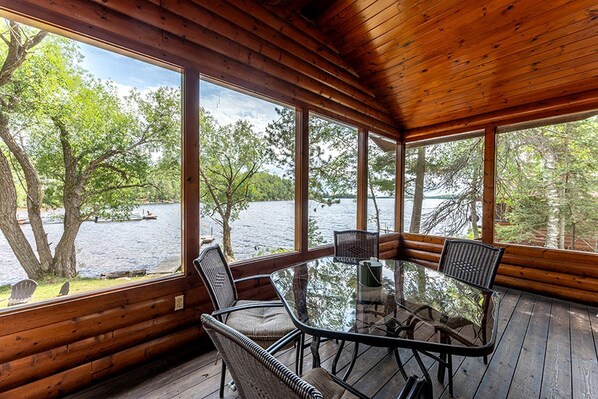 A wooden cabin with a glass table and chairs, overlooking a lake. - Lakeside Cabin Rental for Unforgettable Family Glamping Escapes to Ely, Minnesota (Ely)