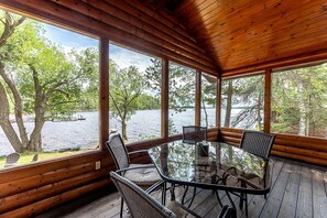 A wooden cabin with a glass table and chairs, overlooking a lake. - Lakeside Cabin Rental for Unforgettable Family Glamping Escapes to Ely, Minnesota (Ely)