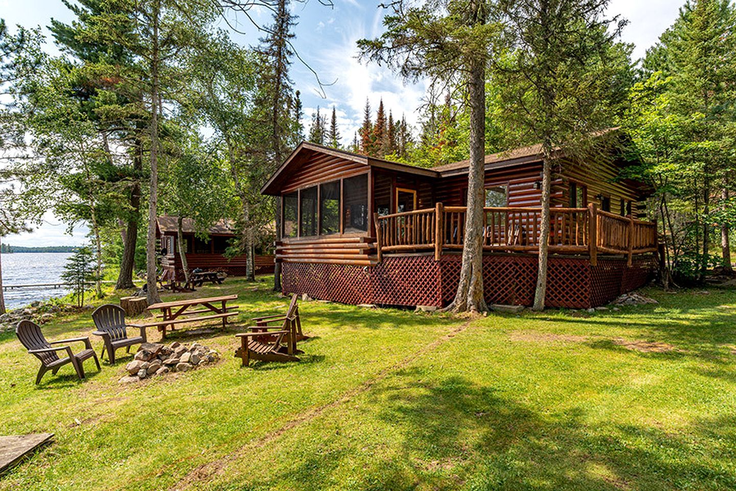 Une cabane dotée d’une terrasse, entourée d’arbres et bordée par un lac.