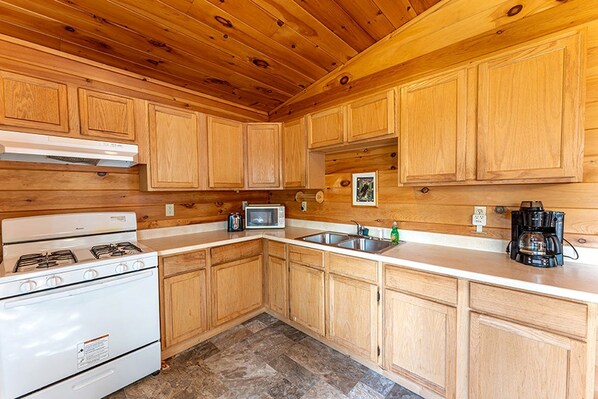 A kitchen with wooden cabinets, a stove, a microwave, a coffee maker, and a sink. - Lakeside Cabin Rental for Unforgettable Family Glamping Escapes to Ely, Minnesota (Ely)