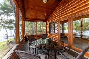 A wooden cabin with a glass dining table and chairs, large windows, and a view of a lake. - Lakeside Cabin Rental for Unforgettable Family Glamping Escapes to Ely, Minnesota (Ely)