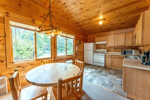 A wooden cabin interior with a round dining table, wooden chairs, a kitchen with a stove, refrigerator, and cabinets. - Lakeside Cabin Rental for Unforgettable Family Glamping Escapes to Ely, Minnesota (Ely)