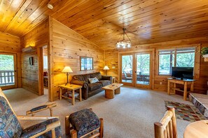A log cabin interior with a sofa, two lamps, a television, and a dining table. - Lakeside Cabin Rental for Unforgettable Family Glamping Escapes to Ely, Minnesota (Ely)