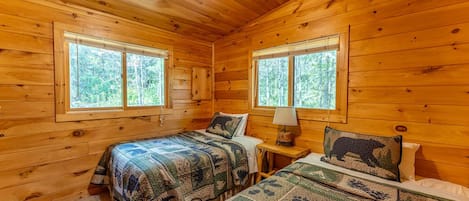 A cabin with two beds, wooden walls, and large windows.