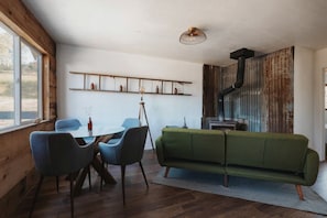Ein gemütliches Zimmer mit Holzboden, einem grünen Sofa, einem Esstisch mit Stühlen, einer Stehlampe und einem rustikalen Kamin.