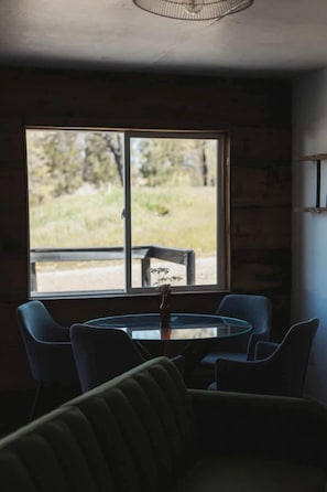 A room with a round table and chairs, a window with a view of greenery, and a ceiling fan. - Peaceful Two Bedroom Cabin on Acres of Private and Secluded Land, Perfect for a Visit to Yosemite National Park (Dunlap)