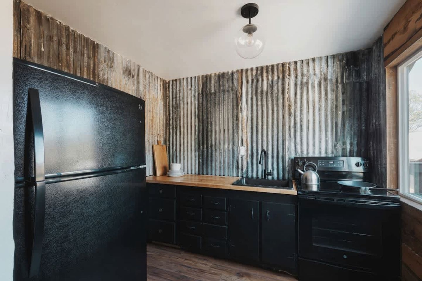 Eine Küche mit einem schwarzen Kühlschrank, Holzschränken, einer Holz Arbeitsplatte, einem Wasserkocher und einem Herd.