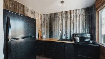 Eine Küche mit einem schwarzen Kühlschrank, Holzschränken, einer Holz Arbeitsplatte, einem Wasserkocher und einem Herd.