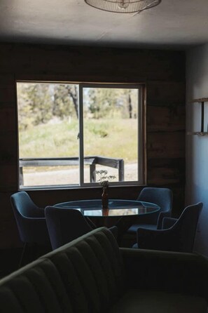 A room with a round table and chairs, a window with a view of greenery, and a ceiling fan. - Peaceful Two Bedroom Cabin on Acres of Private and Secluded Land, Perfect for a Visit to Yosemite National Park (Dunlap)
