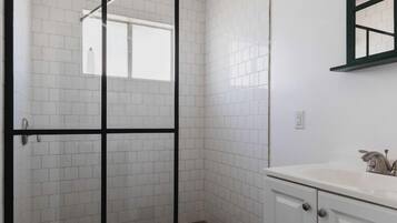 A bathroom with white tiled walls, a glass shower enclosure, a white sink, and a mirror above the sink.