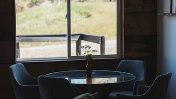 A room with a round table and chairs, a window with a view of greenery, and a ceiling fan.