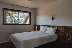 A bedroom with a single bed, a window with a view of trees, and a wooden headboard. - Peaceful Two Bedroom Cabin on Acres of Private and Secluded Land, Perfect for a Visit to Yosemite National Park (Dunlap)