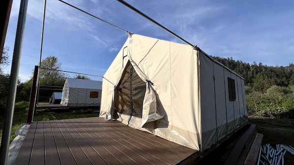 A tent with a ladder, a wooden deck, and a forested background.