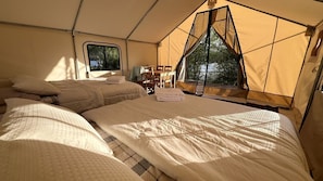 A tented accommodation with two beds, a table, chairs, and a window.