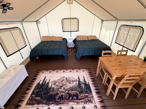Una carpa con dos camas, una mesa y un tapete con diseño de montaña y oso.
