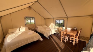 A tented accommodation with two beds, a table, and chairs.