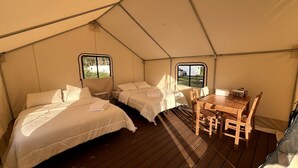 A tented accommodation with two beds, a table, and chairs.