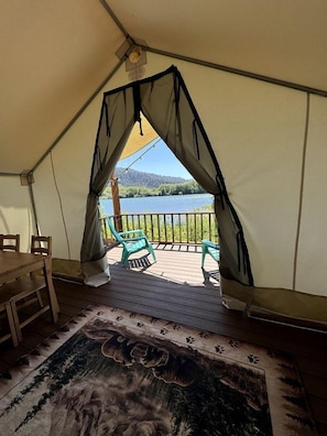 Alojamiento en carpa con vista a un lago, una terraza de madera y un comedor.