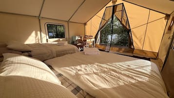 A tented accommodation with two beds, a table, chairs, and a window.