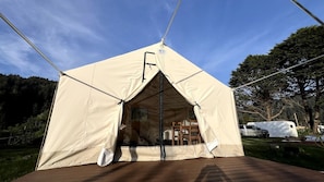 A tent with a door and a window, a wooden deck, and a vehicle in the background.