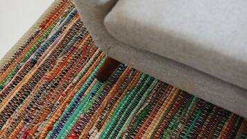 A portion of a room with a grey upholstered armchair and a multicolored striped rug.