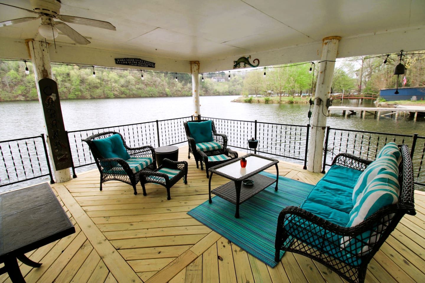 A covered deck with wicker furniture, a table, and a view of a lake.