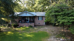 A single-story brick house with a front porch, surrounded by trees and a grassy yard. - Modern Lake House near Hot Springs National Park in Arkansas, Complete with Private Dock and Woodburning Stove (Hot Springs)