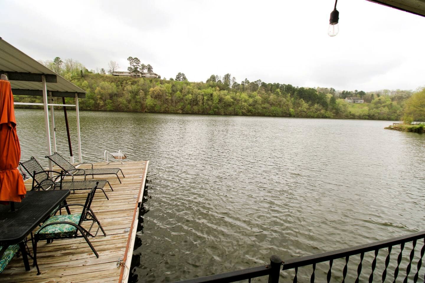 A wooden dock with chairs and a table, overlooking a calm lake with trees in the background.