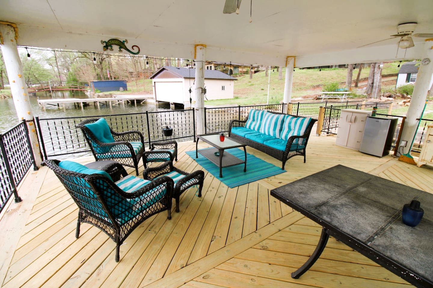 A covered outdoor deck with wicker furniture, a table, and a refrigerator.