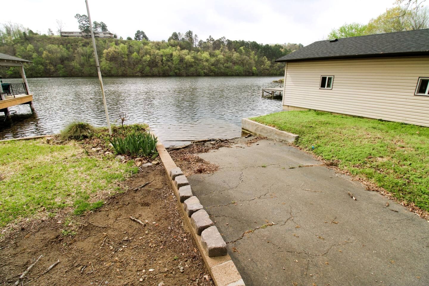 A house by a lake with a dock, a grassy area, and a concrete path leading to the water.