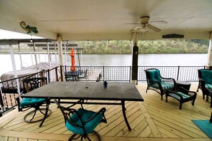Une terrasse couverte avec une table et des chaises, un ventilateur de plafond et une vue sur un lac.
