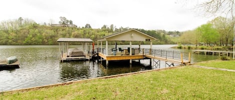 A lakeside dock with a covered seating area and a small boat.