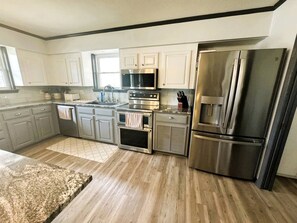 A modern kitchen with stainless steel appliances, light wood flooring, and white cabinetry. - Modern Lake House near Hot Springs National Park in Arkansas, Complete with Private Dock and Woodburning Stove (Hot Springs)