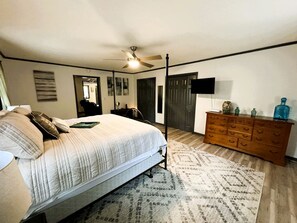 Um quarto com cama, cômoda, ventilador de teto e televisão.