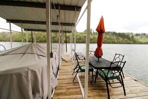 Eine überdachte Terrasse mit Tisch und Stühlen, einem orangefarbenen Sonnenschirm und Blick auf einen See.
