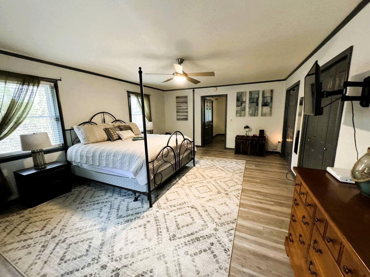 Camera da letto con un letto a baldacchino, una ventola a soffitto, una cassettiera in legno e un'ampia finestra con tende.