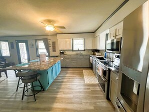 Une cuisine dotée d’un îlot central, de tabourets de bar, d’un réfrigérateur, d’un four, d’un four à micro-ondes et d’un ventilateur de plafond.