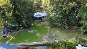 Uma casa rodeada por árvores, um gramado e um pequeno lago.