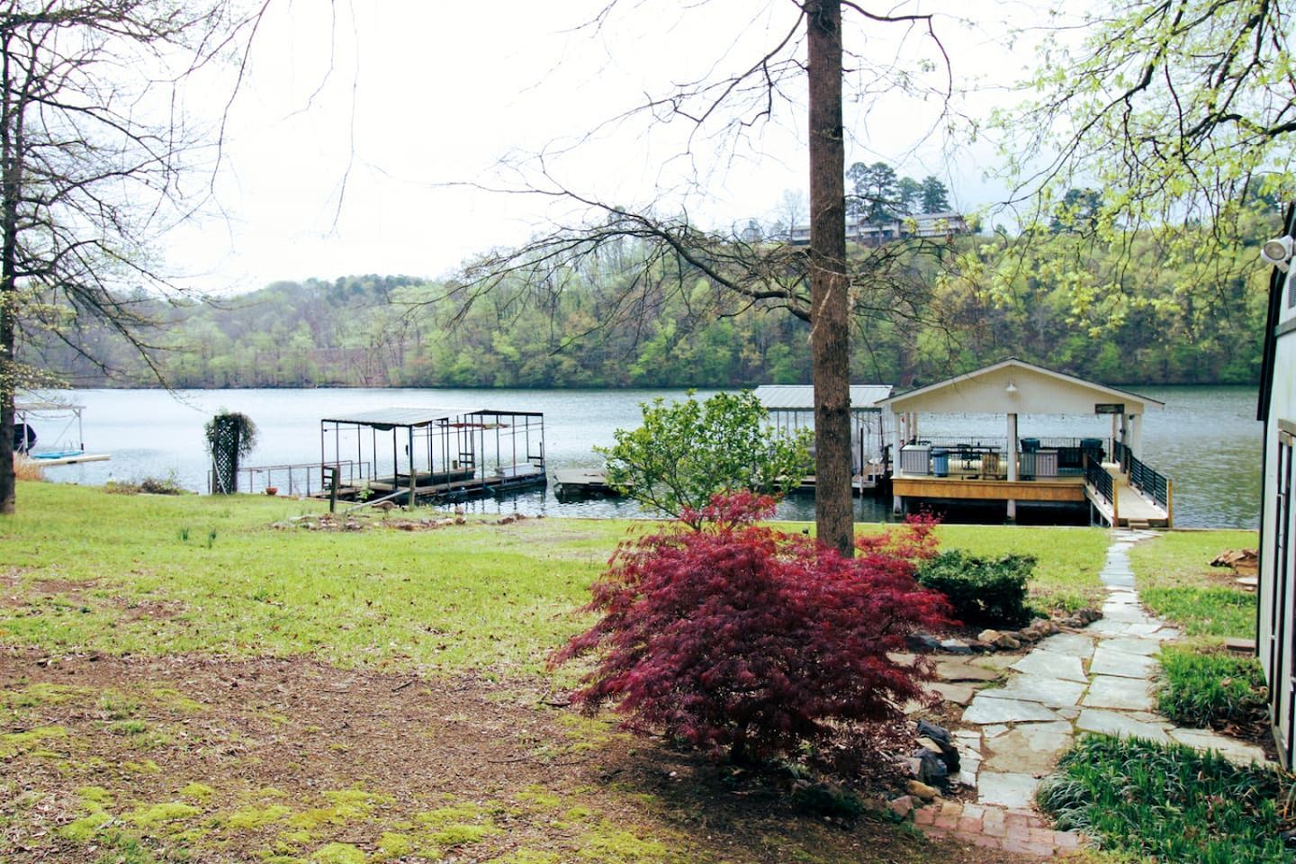 A lakeside property with a dock, a house with a deck, and a stone pathway.