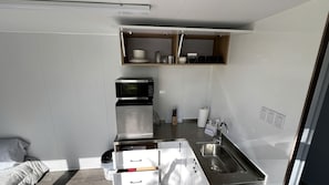 A compact kitchen with a microwave, coffee maker, and a built-in shelf above the sink.