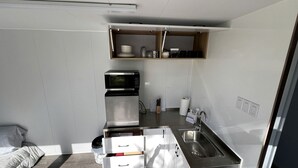 Cocina compacta con microondas, cafetera y estante empotrado sobre el lavabo.