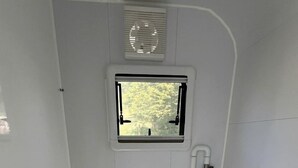 Baño pequeño y blanco con inodoro, una ventana y ventilación.