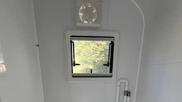 A compact, white bathroom with a toilet, a small window, and a vent.