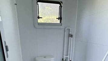 A compact bathroom with a toilet, a window, and a handrail.