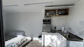 A compact bedroom with a bed, a kitchenette with a microwave, and a small window.