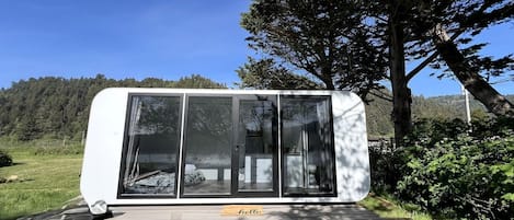 A modern, compact cabin with large glass doors, a wooden deck, and a 'hello' mat.