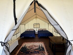 Una carpa con dos camas, una mesa y una alfombra con un paisaje de montaña.