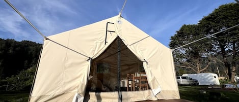 Ein Zelt mit Tür und Fenster, eine Holzterrasse und ein Fahrzeug im Hintergrund.