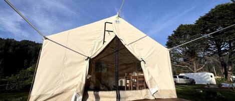 A tent with a door and a window, a wooden deck, and a vehicle in the background.