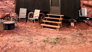 Una pequeña cabaña de madera oscura con una puerta y ventanas, ubicada en un paisaje desértico pedregoso.